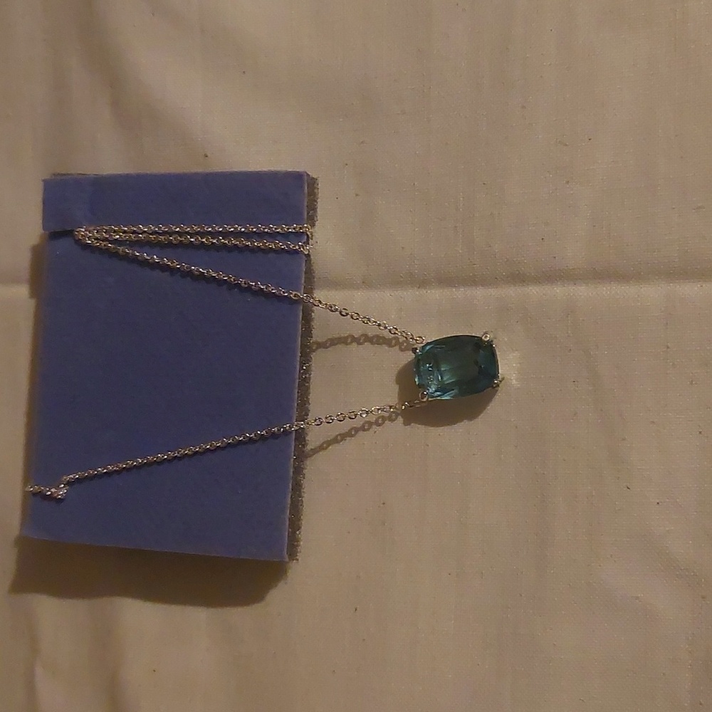 A silver tone chain necklace with a light blue square pendant.